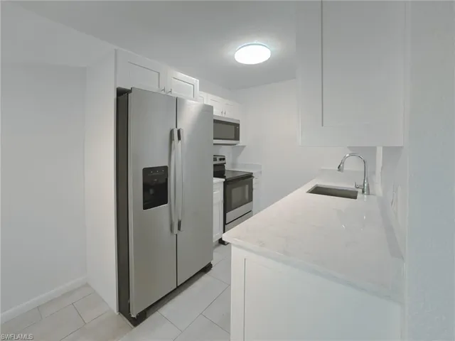 Kitchen featuring light stone counters, appliances with stainless steel finishes, white cabinets, and light tile patterned flooring