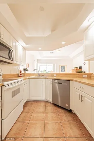 Kitchen with stainless steel appliances, light countertops, a raised ceiling, light tile patterned floors, and recessed lighting