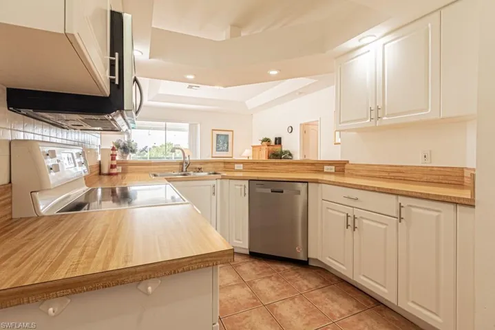 Kitchen with a tray ceiling, white cabinetry, stainless steel dishwasher, light countertops, and recessed lighting