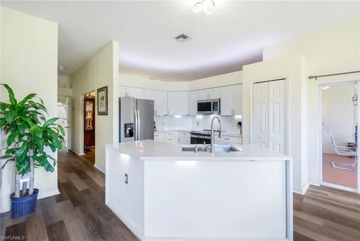 Kitchen with white cabinetry, dark wood-type flooring, appliances with stainless steel finishes, an island with sink, and sink