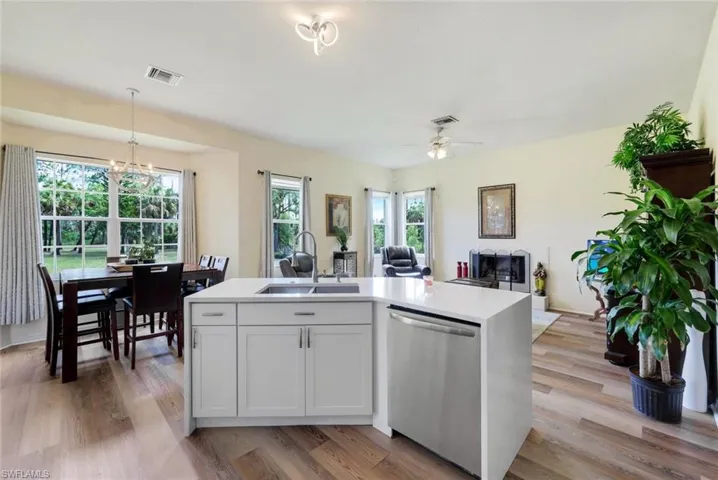 Kitchen featuring stainless steel dishwasher, a center island with sink, light wood-type flooring, hanging light fixtures, and sink