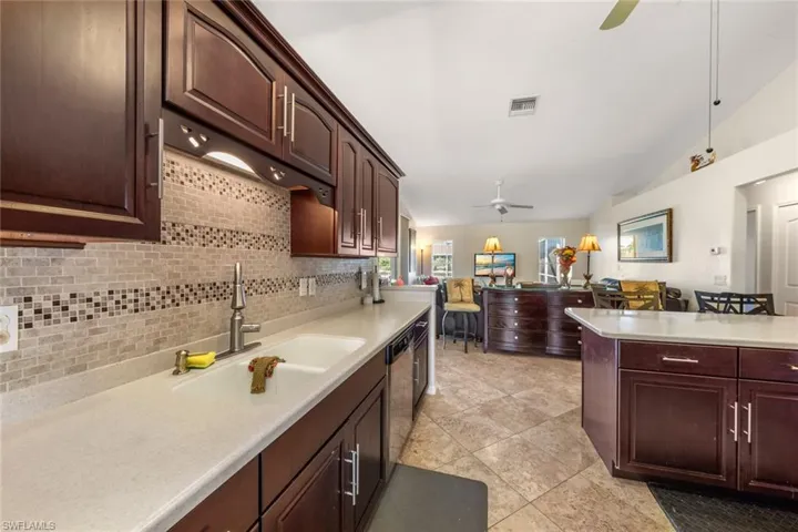 Kitchen featuring decorative backsplash, ceiling fan, sink, light tile patterned floors, and lofted ceiling