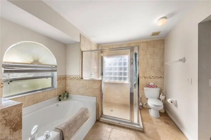 Bathroom featuring toilet, tile walls, and plus walk in shower