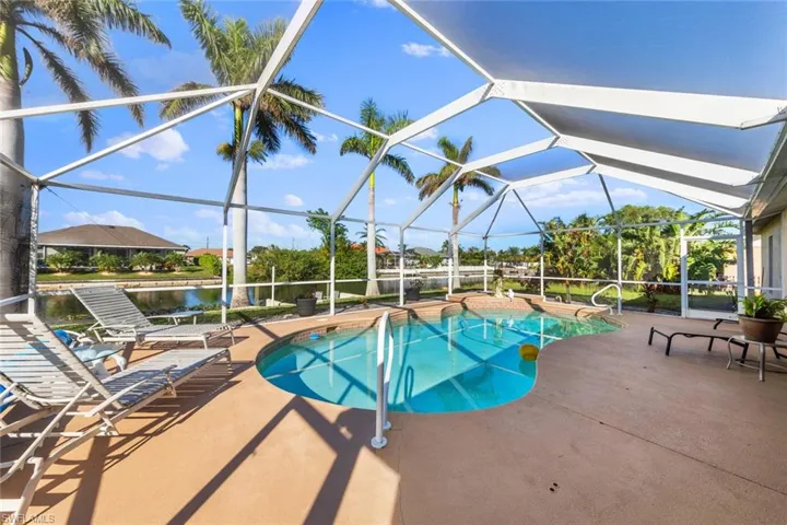 View of pool with a patio area, a water view, and glass enclosure