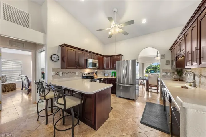 Kitchen featuring high vaulted ceiling, a kitchen breakfast bar, sink, ceiling fan, and stainless steel appliances