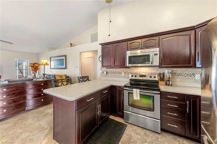 Kitchen with kitchen peninsula, decorative backsplash, stainless steel appliances, and high vaulted ceiling
