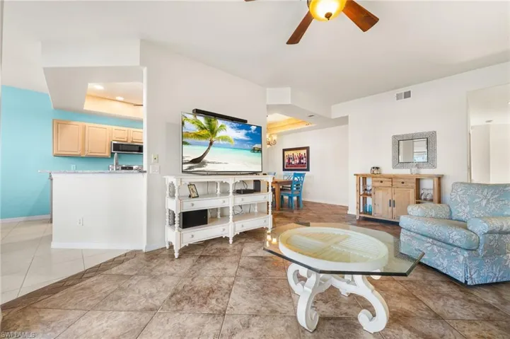 Living room with ceiling fan, light tile patterned flooring, and a tray ceiling