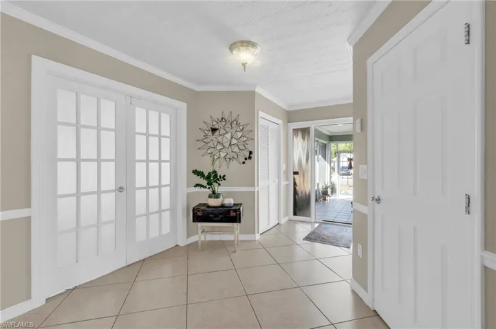 Foyer with light tile patterned floors, a textured ceiling, french doors, and crown molding