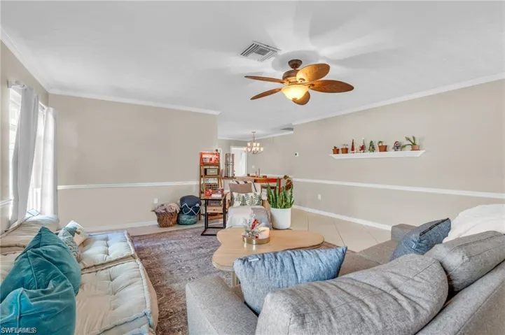 Living room featuring ornamental molding, visible vents, ceiling fan with notable chandelier, and a healthy amount of sunlight