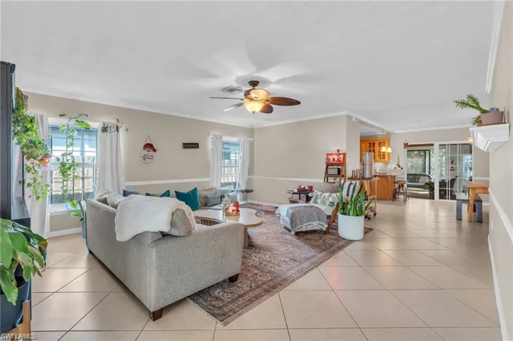 Living area featuring ceiling fan, light tile patterned flooring, and ornamental molding