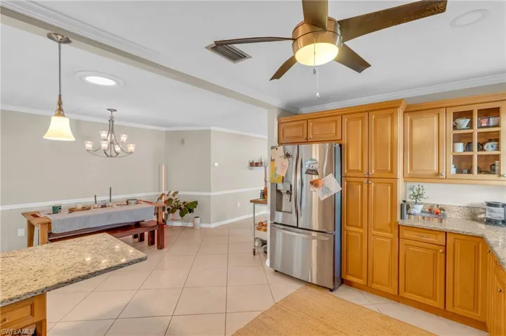 Kitchen with light stone countertops, pendant lighting, stainless steel refrigerator with ice dispenser, and ornamental molding