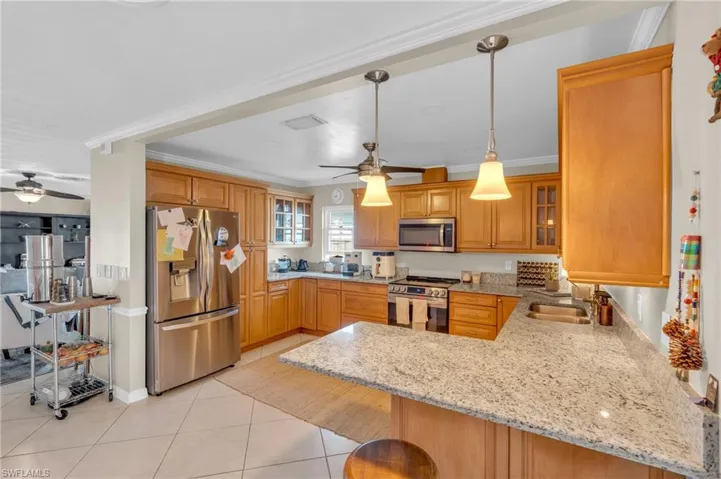 Kitchen with crown molding, hanging light fixtures, a kitchen bar, kitchen peninsula, and stainless steel appliances