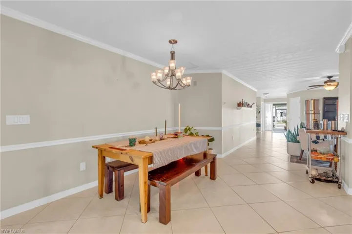 Tiled dining space with ceiling fan with notable chandelier and ornamental molding