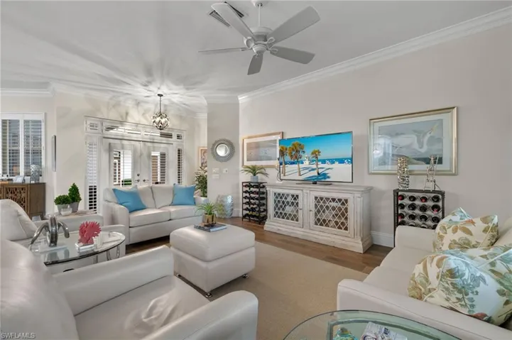 Living room with ceiling fan with notable chandelier, french doors, ornamental molding, and wood-type flooring