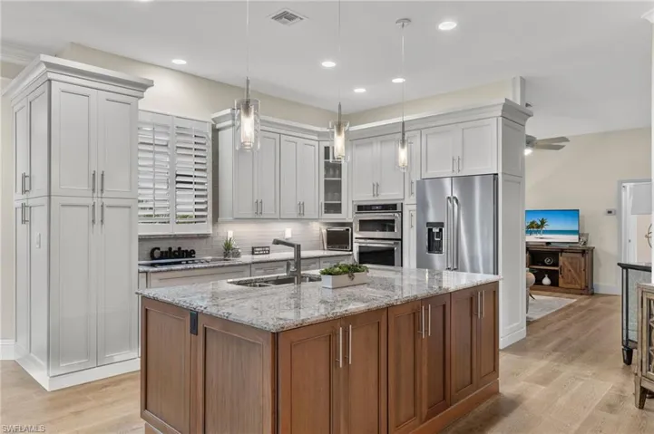 Kitchen with white cabinetry, light hardwood / wood-style flooring, ceiling fan, light stone countertops, and appliances with stainless steel finishes