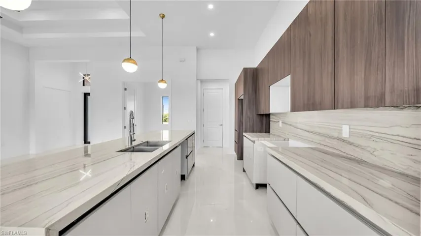 Kitchen with modern cabinets, light stone counters, decorative light fixtures, a spacious island, and two tone cabinets