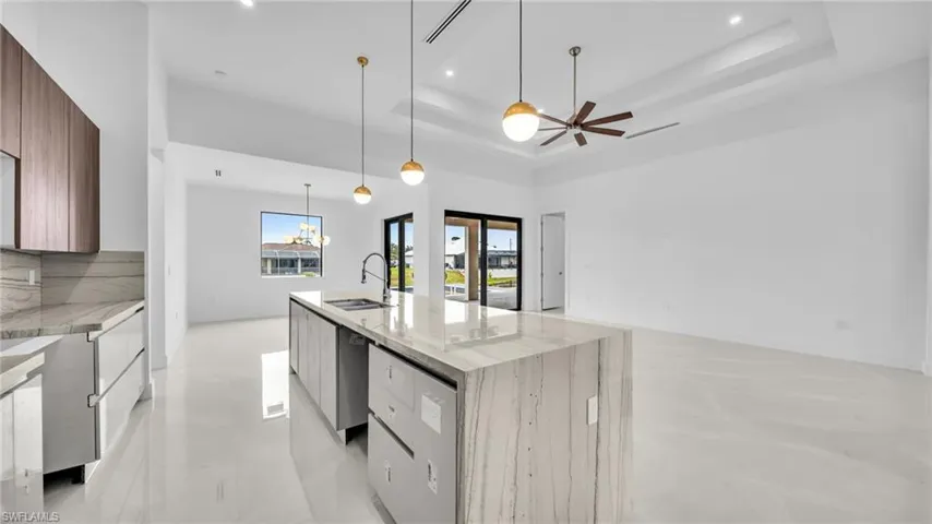 Kitchen with light stone countertops, modern cabinets, suspended lighting, a center island with sink, and open floor plan