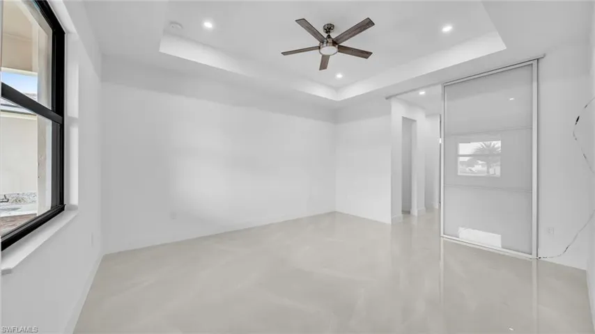Unfurnished bedroom featuring concrete flooring, ceiling fan, recessed lighting, and a raised ceiling