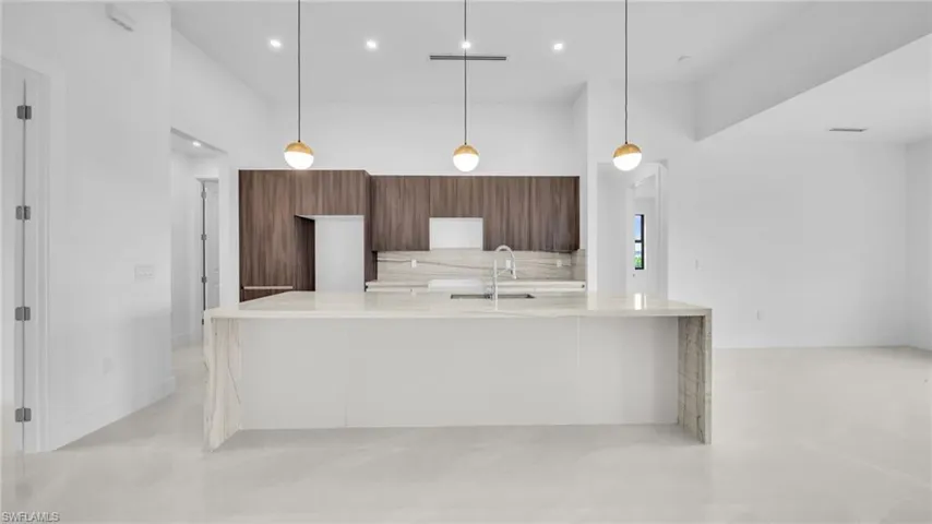 Kitchen featuring modern cabinets, light stone counters, an island with sink, pendant lighting, and a high ceiling