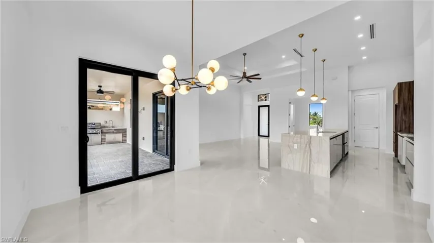 Kitchen with a chandelier, light stone countertops, ceiling fan, an island with sink, and a tray ceiling
