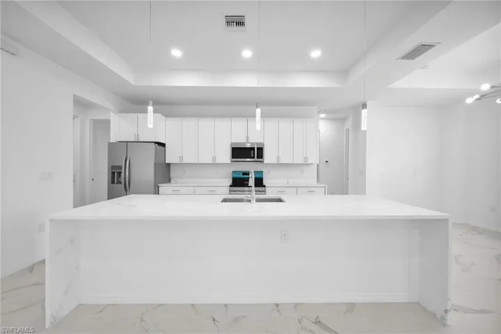Spacious kitchen featuring a large waterfall-edge island with white countertops, white shaker cabinetry, stainless steel appliances, and pendant lighting