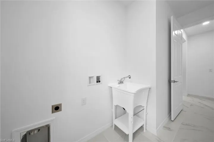 Utility room featuring a white laundry sink with a chrome faucet, white baseboards, and light-toned tile flooring
