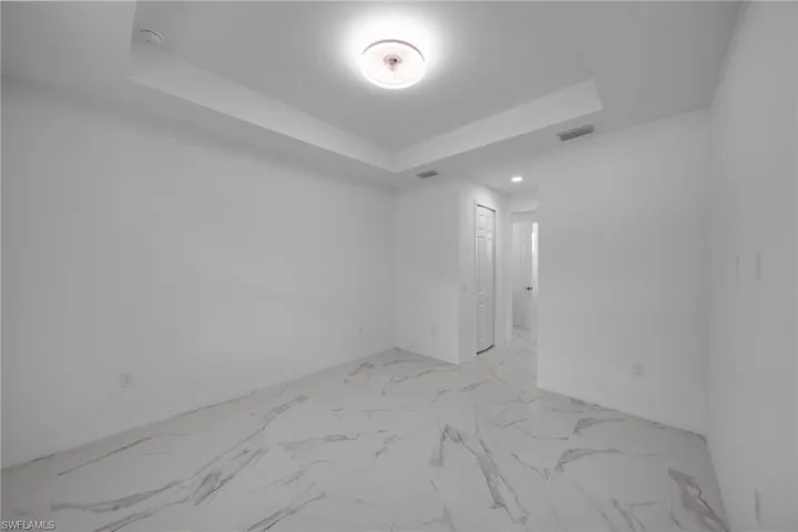 MASTER Spacious room featuring large format tile flooring with distinctive veining, a tray ceiling, and a flush mount ceiling fixture