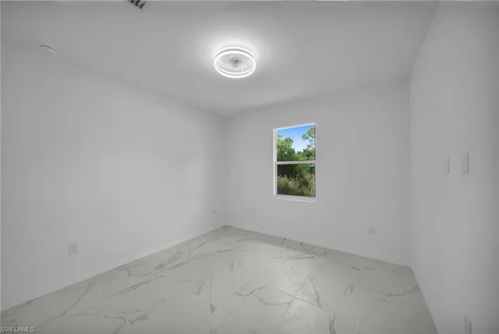 GUEST ROOM 2Bright room featuring white walls, large format tile flooring, a modern flush-mount ceiling light, and a single window with exterior landscaping