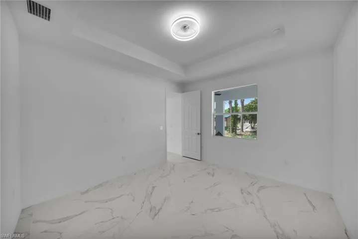 MASTER Spacious interior room featuring large format marble-look tile flooring, white walls, a tray ceiling with a modern flush-mount light fixture, and a window providing natural light
