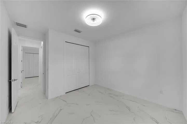 GUEST Room 2 featuring white walls, white bifold closet doors, and white marble-look tile flooring