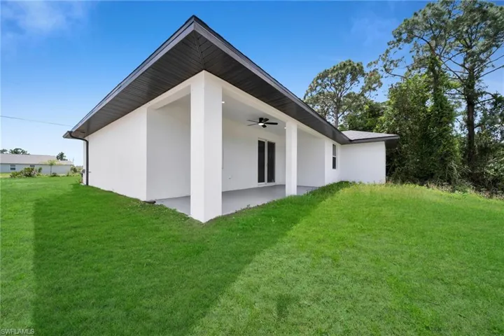 Rear exterior featuring a covered patio with a ceiling fan, white stucco finish, dark roofline, and a lush green lawn