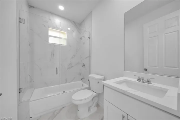 GUEST BATHROOM Bathroom featuring a white bathtub with clear glass shower enclosure, white vanity with integrated sink, and large wall-mounted mirror