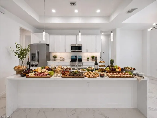 Spacious kitchen featuring a large waterfall island with a light-toned countertop, white cabinetry, integrated stainless steel appliances, and recessed lighting