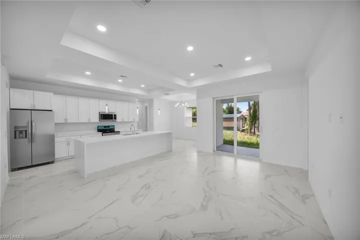 Open-concept kitchen and living area featuring white cabinetry, stainless steel appliances, and a central island