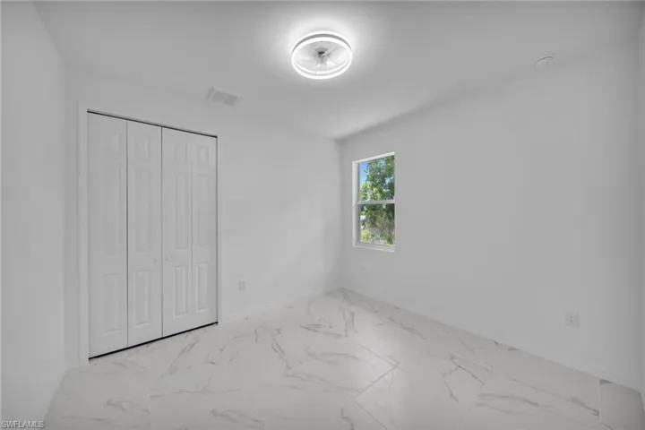 GUEST BEDROOM 1 Room featuring white walls, large format tile flooring, a single window, and bi-fold closet doors