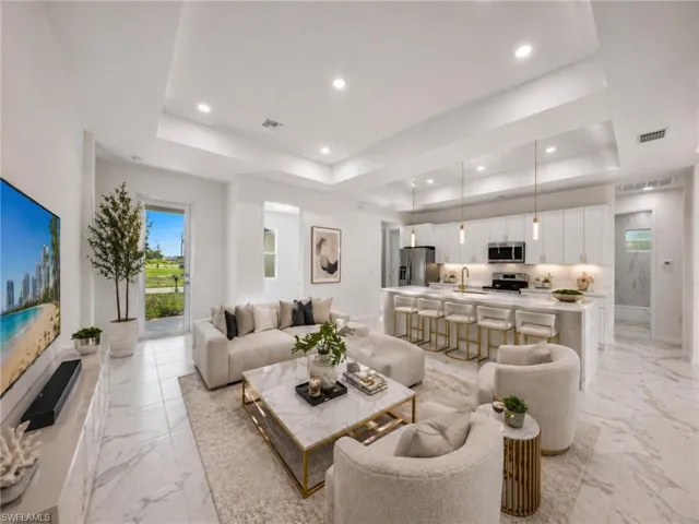 Open-concept interior featuring light-toned large format tile flooring, a tray ceiling with recessed lighting, and a kitchen island with pendant lighting