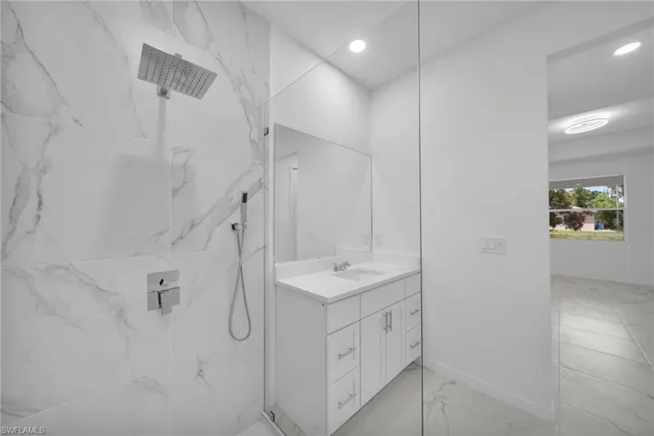 Frameless glass shower enclosure featuring a square rainfall showerhead and hand-held sprayer