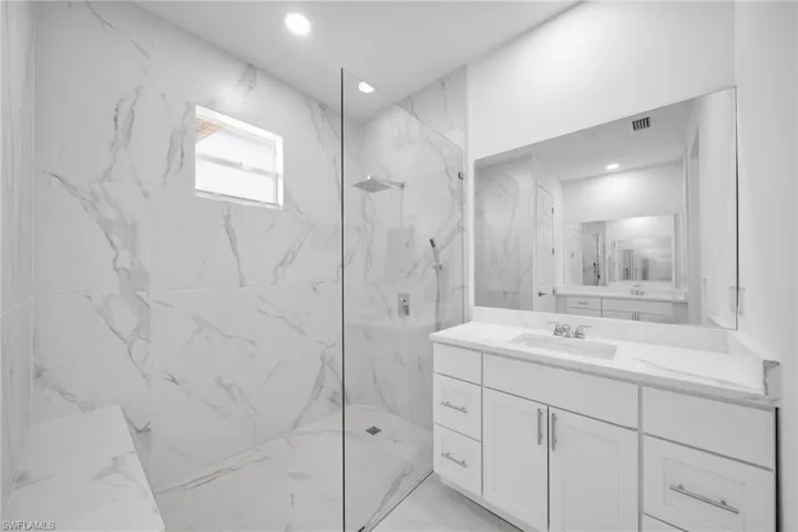 Spacious bathroom featuring a white vanity with an integrated sink and a large frameless mirror