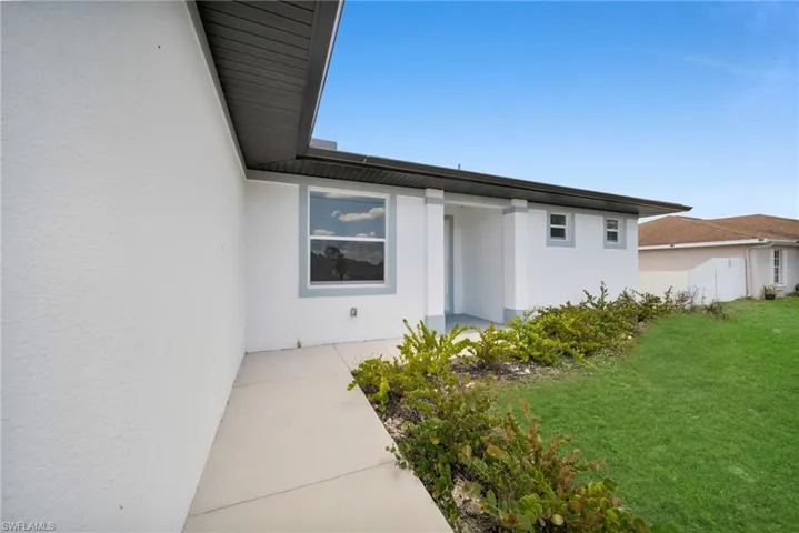 Exterior featuring a stucco facade, covered entryway, contrasting trim, a concrete walkway, and a manicured lawn with shrubbery