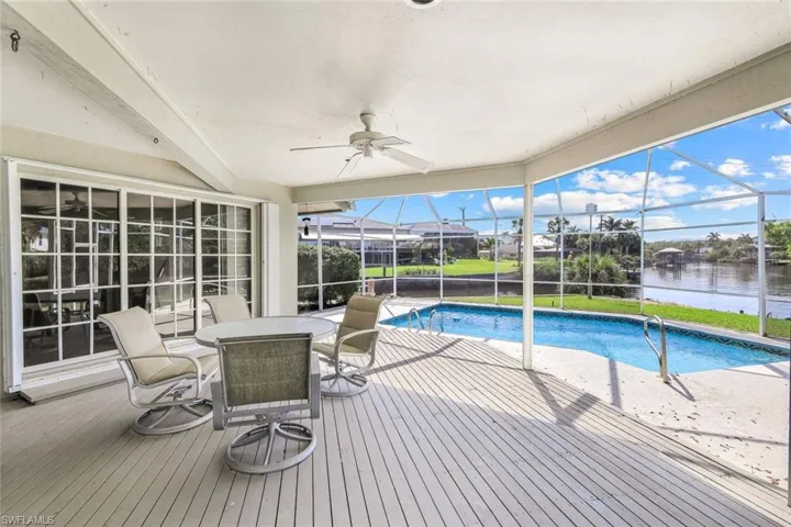 Pool featuring a water view, a ceiling fan, glass enclosure, a patio, and outdoor dining area