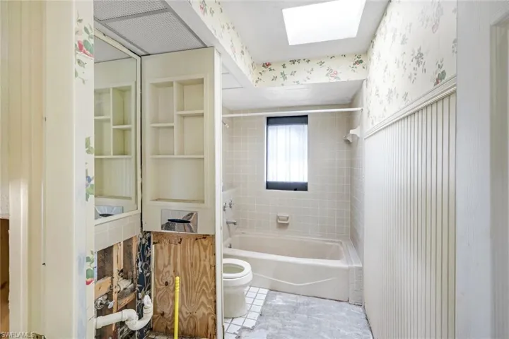 Full bathroom with toilet, a skylight, wallpapered walls, and shower / bathing tub combination