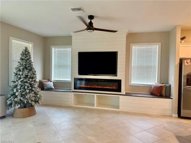 Unfurnished living room with a ceiling fan, light tile patterned floors, and a large fireplace