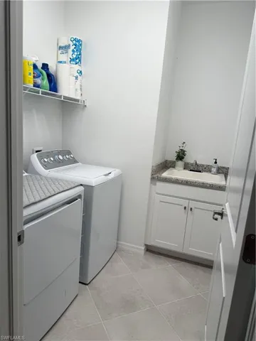 Washroom with a sink, washing machine and dryer, light tile patterned floors, and baseboards