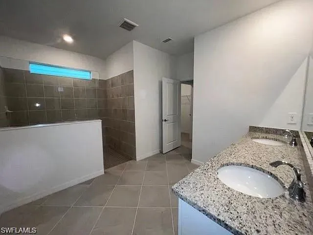 Full bath featuring a walk in shower, double vanity, tile patterned flooring, and baseboards