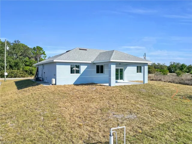 Back of property featuring a lawn, stucco siding, roof with shingles, and a patio area