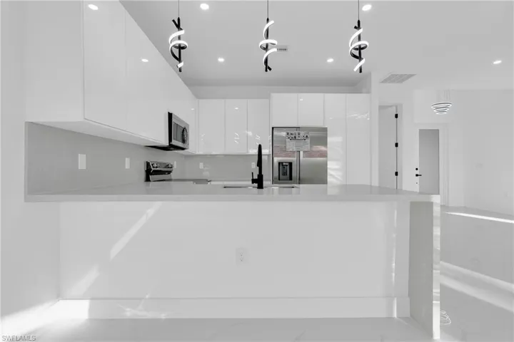 Kitchen featuring white cabinets, a peninsula, modern cabinets, stainless steel refrigerator with ice dispenser, and light stone countertops