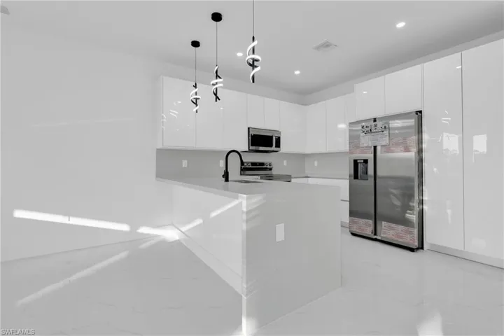 Kitchen featuring modern cabinets, white cabinets, stainless steel appliances, a peninsula, and decorative light fixtures