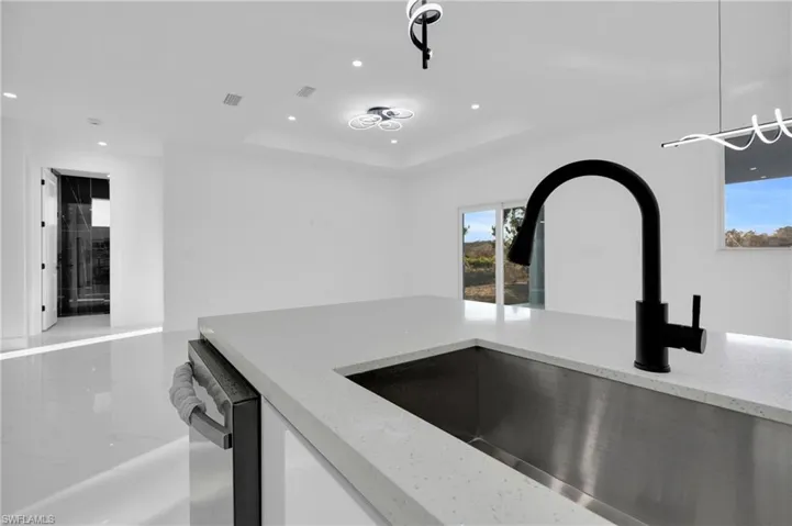 Kitchen with light stone countertops, a raised ceiling, recessed lighting, white cabinetry, and stainless steel dishwasher