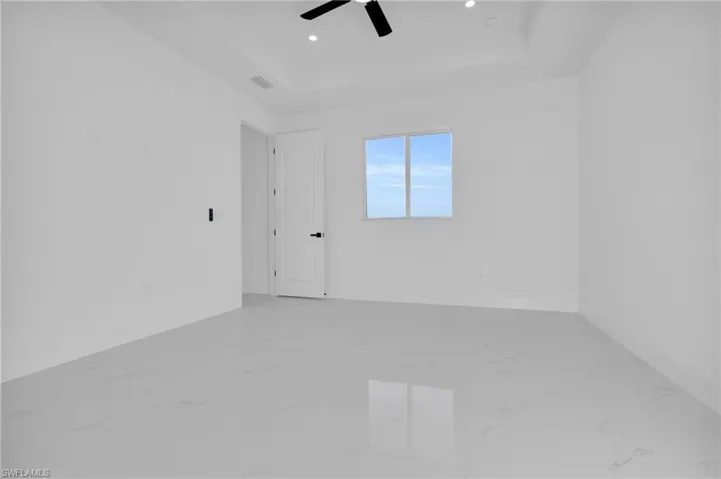 Empty room featuring a raised ceiling, light marble finish flooring, a ceiling fan, and recessed lighting