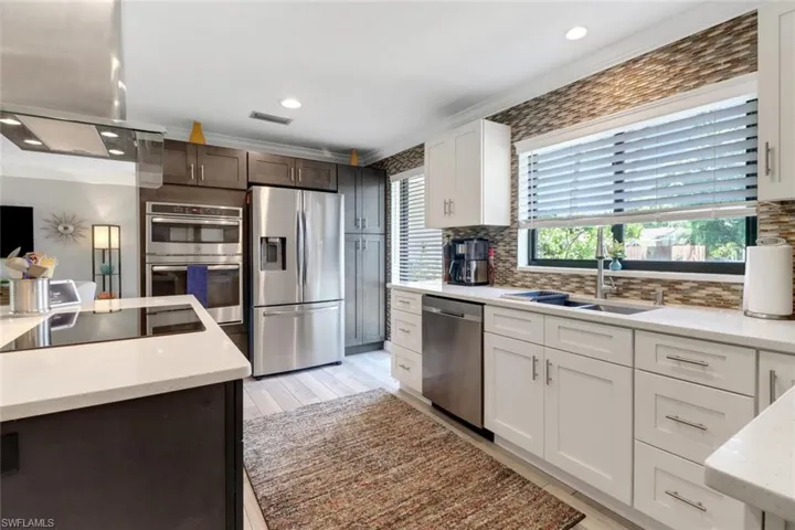 Kitchen featuring stainless steel appliances, island range hood, tasteful backsplash, white cabinetry, and light wood-style floors